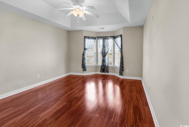 empty room with a tray ceiling, wood finished floors, visible vents, and baseboards