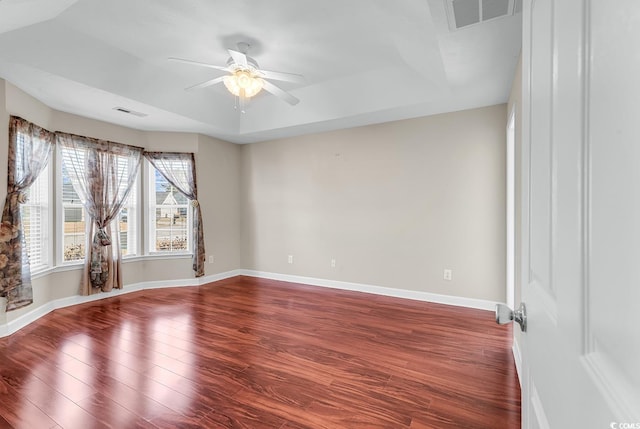 unfurnished room featuring ceiling fan, wood finished floors, visible vents, baseboards, and a tray ceiling