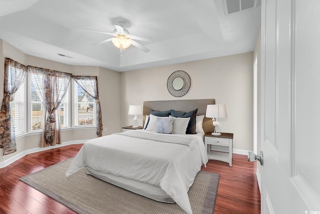 bedroom with a tray ceiling, visible vents, baseboards, and wood finished floors