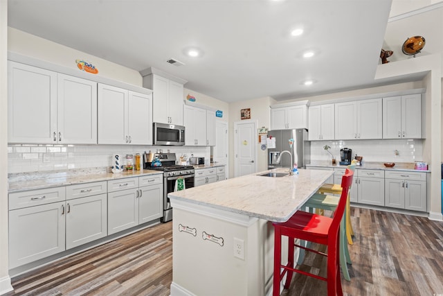 kitchen featuring tasteful backsplash, a center island with sink, a kitchen bar, appliances with stainless steel finishes, and light stone counters