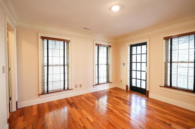 empty room featuring wood-type flooring, a healthy amount of sunlight, and crown molding