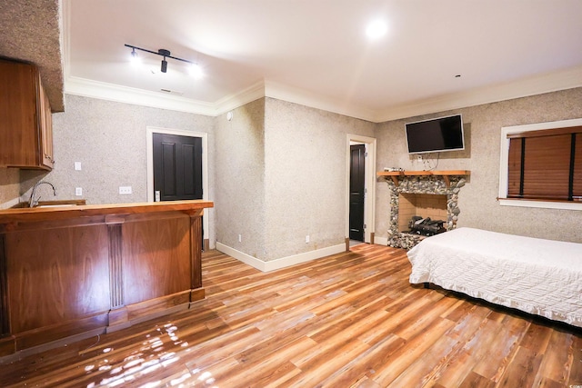 unfurnished bedroom featuring sink, crown molding, track lighting, light hardwood / wood-style floors, and a stone fireplace