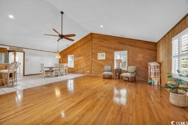 unfurnished room with wooden walls, plenty of natural light, vaulted ceiling, and light wood-type flooring