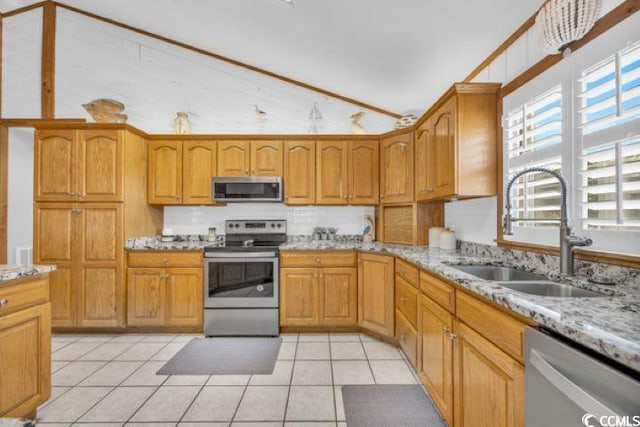 kitchen featuring appliances with stainless steel finishes, light stone counters, vaulted ceiling, sink, and light tile patterned floors