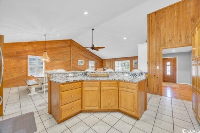 kitchen featuring ceiling fan, light tile patterned floors, light stone countertops, and wooden walls