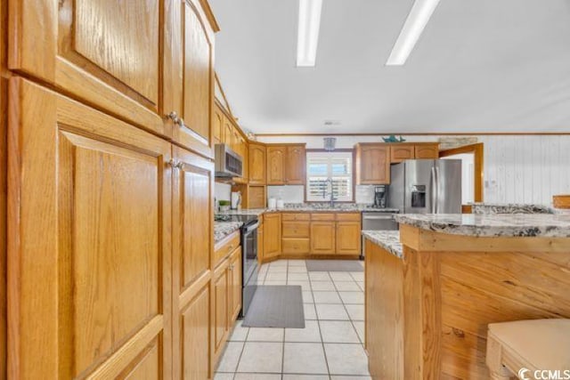 kitchen featuring sink, wooden walls, light tile patterned floors, appliances with stainless steel finishes, and light stone counters