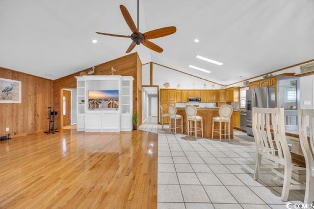 unfurnished living room featuring wooden walls, ceiling fan, vaulted ceiling, and ornamental molding