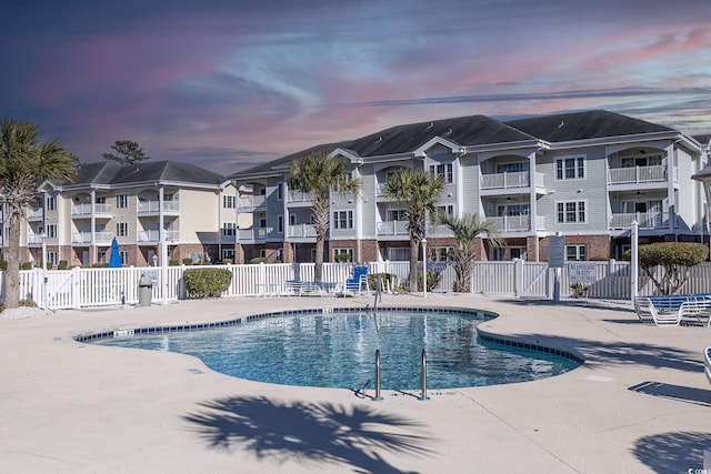 pool at dusk featuring a residential view, fence, a community pool, and a patio