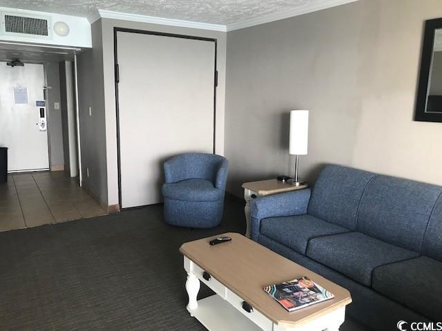 living room with dark carpet, ornamental molding, and a textured ceiling