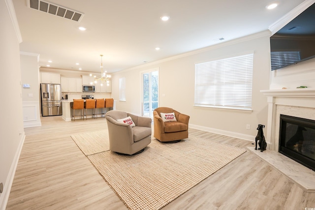 living room with a notable chandelier, ornamental molding, a premium fireplace, and light wood-type flooring