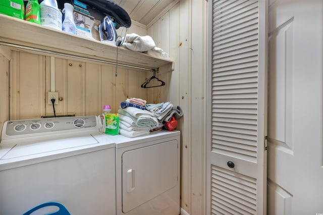 clothes washing area featuring wood walls and washing machine and dryer