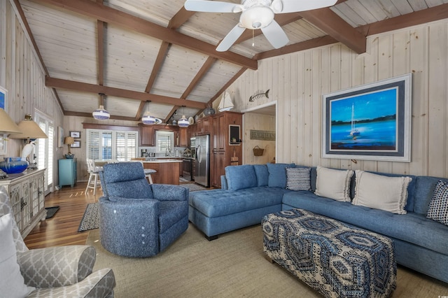 living room featuring vaulted ceiling with beams, ceiling fan, light hardwood / wood-style floors, and wood walls