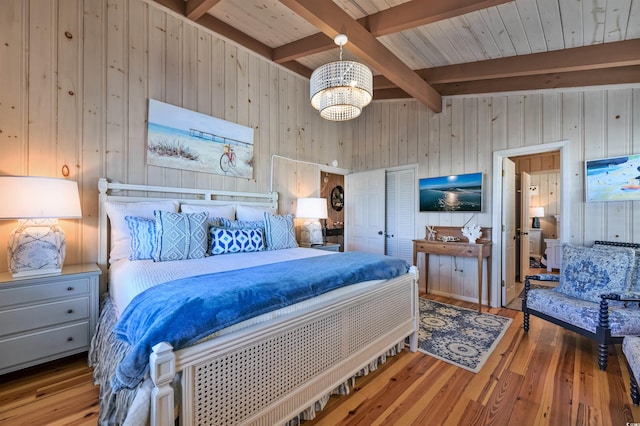 bedroom featuring wood walls, light hardwood / wood-style flooring, beamed ceiling, and a notable chandelier