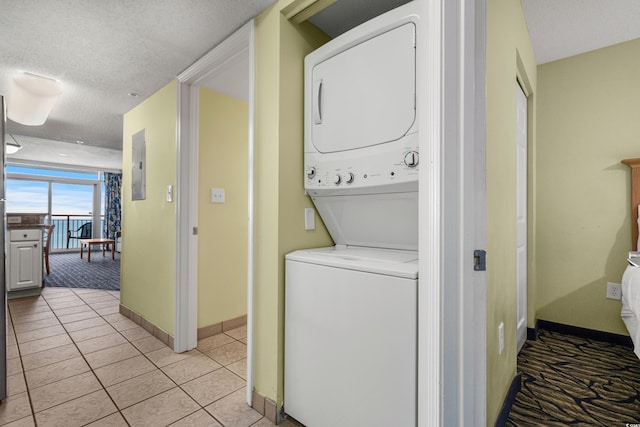 laundry area with light tile patterned floors, a textured ceiling, electric panel, and stacked washer / dryer