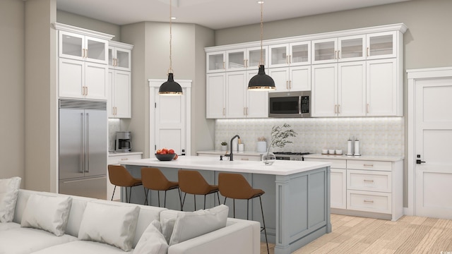 kitchen with decorative light fixtures, a kitchen island with sink, appliances with stainless steel finishes, a breakfast bar area, and white cabinets