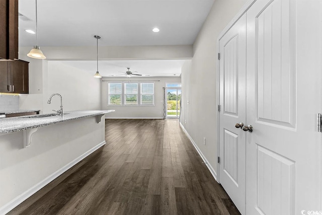 kitchen featuring a breakfast bar, ceiling fan, sink, pendant lighting, and dark hardwood / wood-style floors