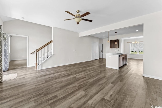 unfurnished living room with sink, dark wood-type flooring, and ceiling fan with notable chandelier