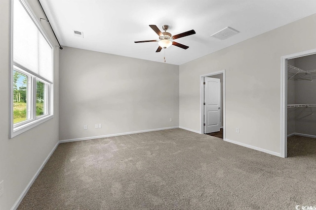 unfurnished bedroom featuring a walk in closet, dark carpet, a closet, and ceiling fan