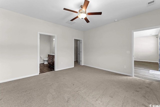 unfurnished bedroom featuring dark colored carpet, ensuite bath, ceiling fan, a spacious closet, and a closet