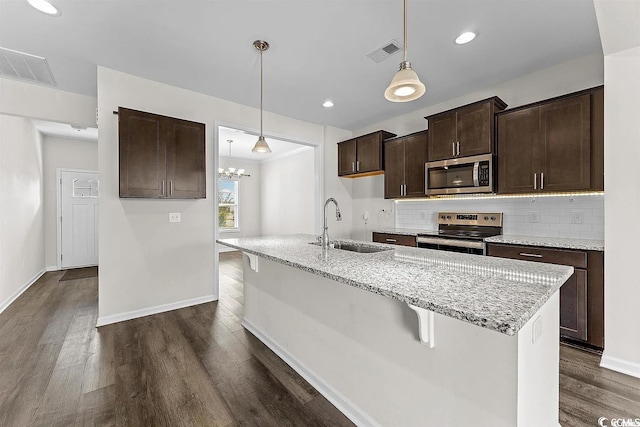 kitchen featuring sink, light stone countertops, appliances with stainless steel finishes, decorative light fixtures, and dark brown cabinetry