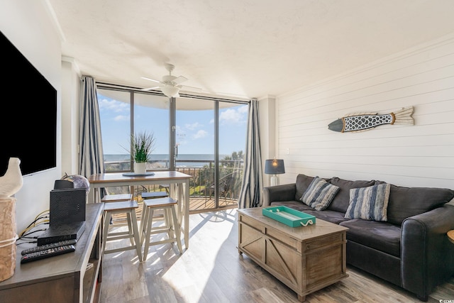 living room featuring hardwood / wood-style floors, ceiling fan, a water view, and a wall of windows