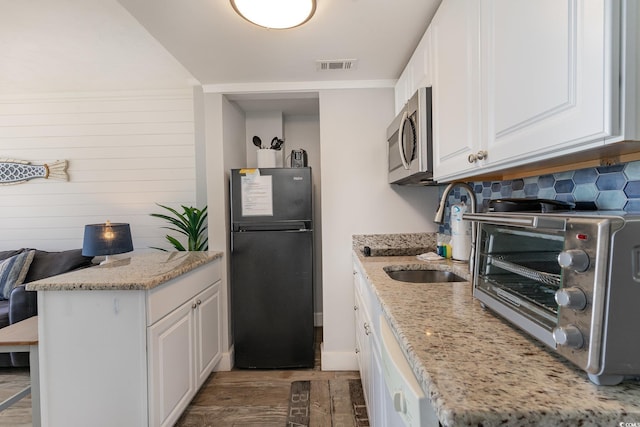 kitchen featuring black fridge, sink, white cabinets, and light stone countertops