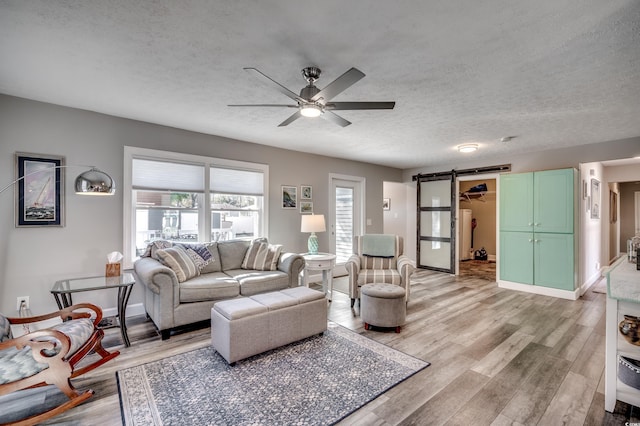 living room with a barn door, ceiling fan, light hardwood / wood-style flooring, and a textured ceiling