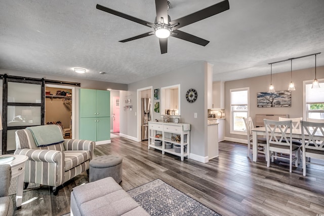 living room with a textured ceiling, ceiling fan, a barn door, and dark wood-type flooring