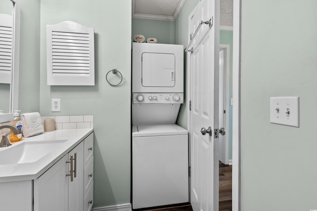 clothes washing area with ornamental molding, a textured ceiling, stacked washer and clothes dryer, and sink