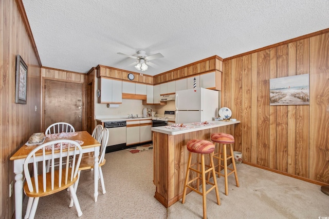 kitchen with kitchen peninsula, white appliances, white cabinetry, and wooden walls