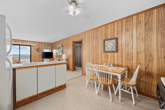 dining room with a textured ceiling, ceiling fan, and wooden walls