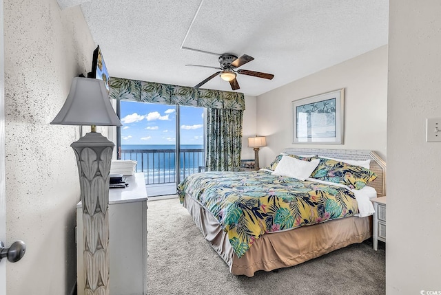 carpeted bedroom with access to exterior, a textured ceiling, a water view, and ceiling fan