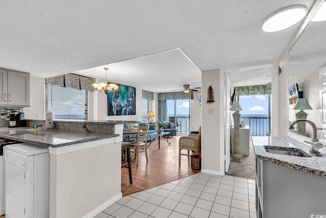 kitchen with gray cabinetry, a breakfast bar, ceiling fan with notable chandelier, sink, and light tile patterned floors