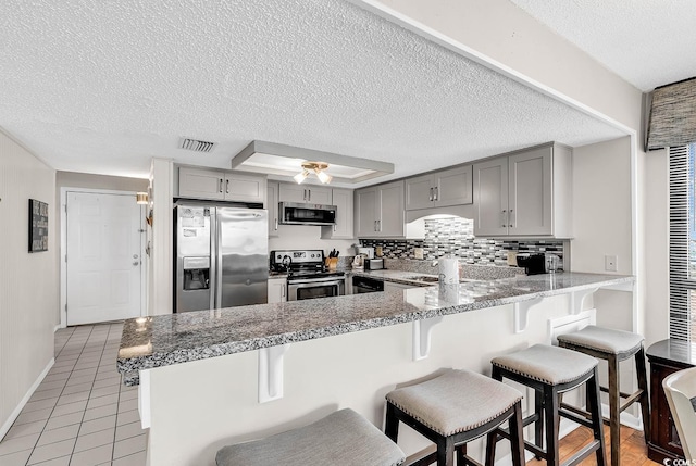 kitchen with a kitchen breakfast bar, kitchen peninsula, gray cabinetry, and appliances with stainless steel finishes