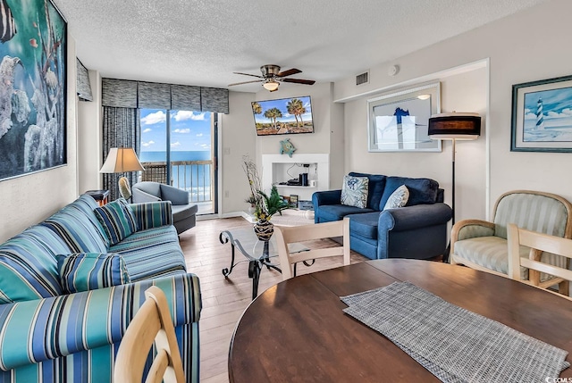 living area with ceiling fan, a textured ceiling, visible vents, baseboards, and light wood-style floors