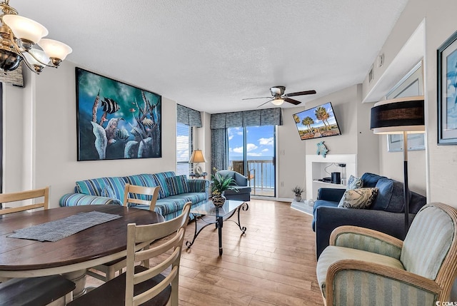 living room with ceiling fan with notable chandelier, light hardwood / wood-style floors, and a textured ceiling