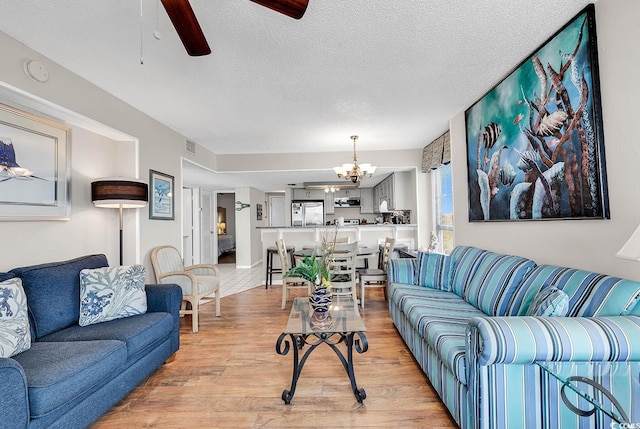 living room with light wood-type flooring, a textured ceiling, and ceiling fan with notable chandelier