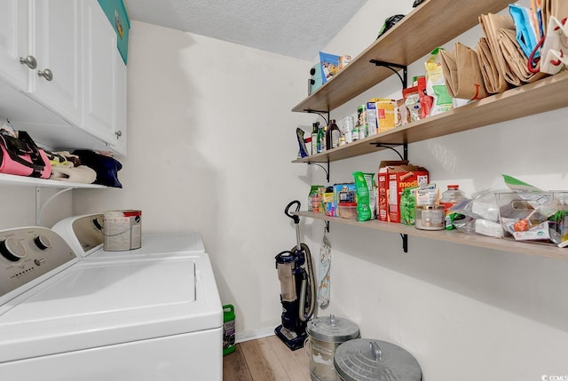 laundry room with cabinets, washing machine and dryer, a textured ceiling, and light wood-type flooring