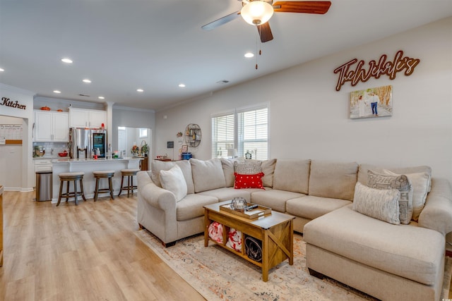 living room featuring ceiling fan, light wood-type flooring, and crown molding