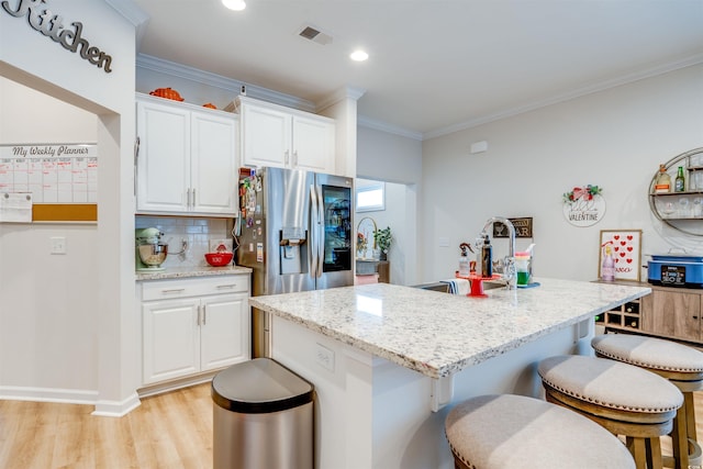 kitchen with stainless steel refrigerator with ice dispenser, white cabinets, and an island with sink