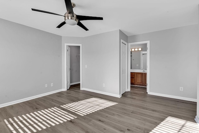 unfurnished bedroom featuring hardwood / wood-style floors, a walk in closet, ensuite bath, ceiling fan, and a closet