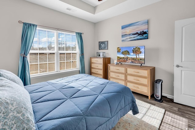 bedroom with a raised ceiling and wood-type flooring