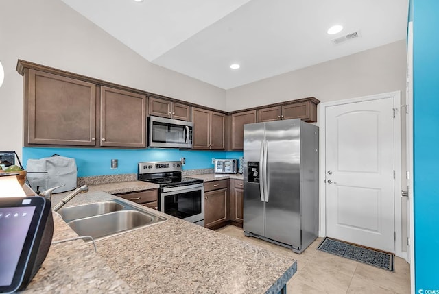 kitchen with sink, vaulted ceiling, light tile patterned floors, appliances with stainless steel finishes, and dark brown cabinetry