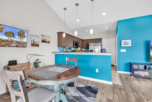 kitchen with dark brown cabinetry, stainless steel appliances, high vaulted ceiling, pendant lighting, and light hardwood / wood-style floors