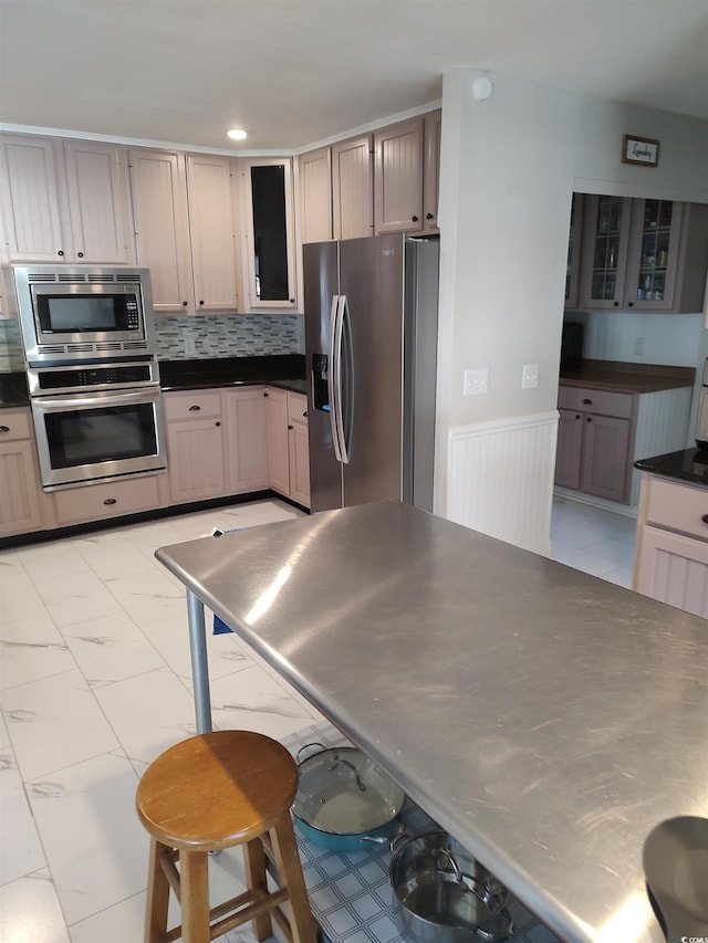 kitchen with marble finish floor, dark countertops, decorative backsplash, appliances with stainless steel finishes, and glass insert cabinets