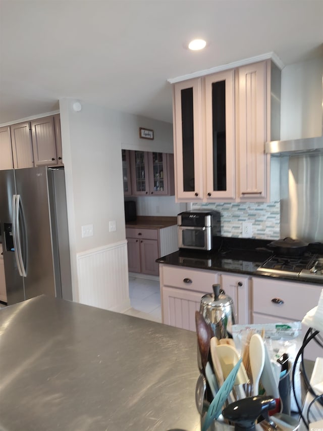 kitchen featuring appliances with stainless steel finishes, wall chimney range hood, backsplash, dark countertops, and glass insert cabinets