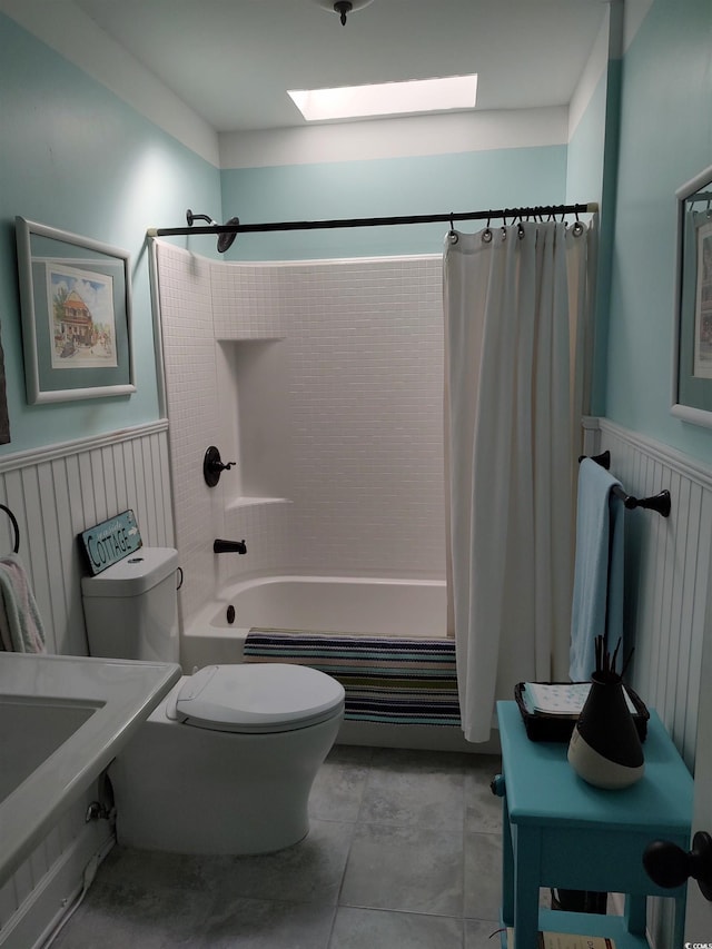 bathroom featuring toilet, a wainscoted wall, a skylight, and shower / tub combo with curtain