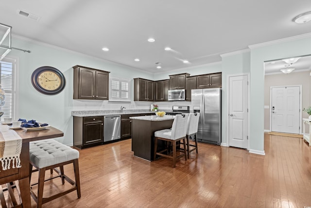 3716 Mackevans Ct, Myrtle Beach, SC 29579 - kitchen featuring appliances with stainless steel finishes, dark brown cabinetry, ornamental molding, a kitchen island, and a kitchen bar