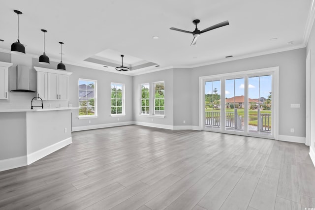 unfurnished living room featuring a wealth of natural light, a raised ceiling, ceiling fan, crown molding, and sink