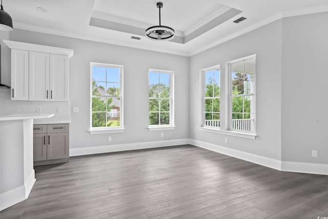 unfurnished dining area featuring a raised ceiling, dark wood-type flooring, crown molding, and an inviting chandelier